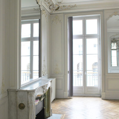 Salon avec parquet en losange. Cheminée en marbre surmontée d'un grand miroir. Moulures sur les murs et plafond.