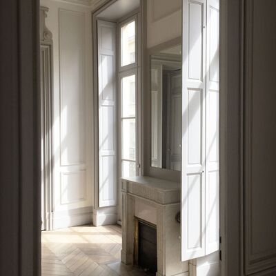 Cheminée grise. Grandes fenêtres. Parquet en bois brut.