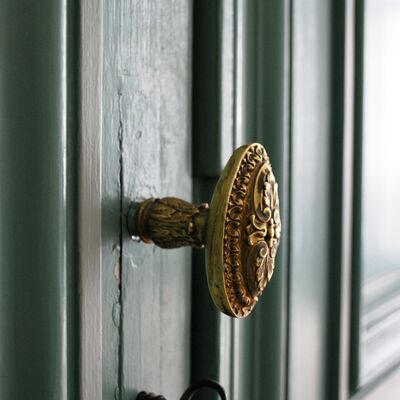 Poignée de porte dorée avec moulures. Porte vert sombre.